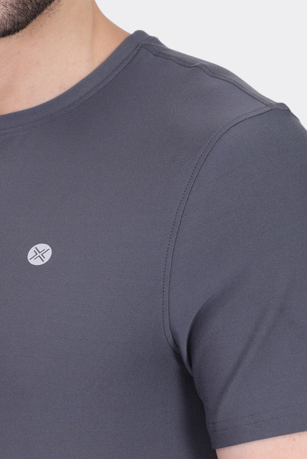 Close-up of a man wearing a dark gray short-sleeve crewneck t-shirt with a small white compass logo on the left chest.